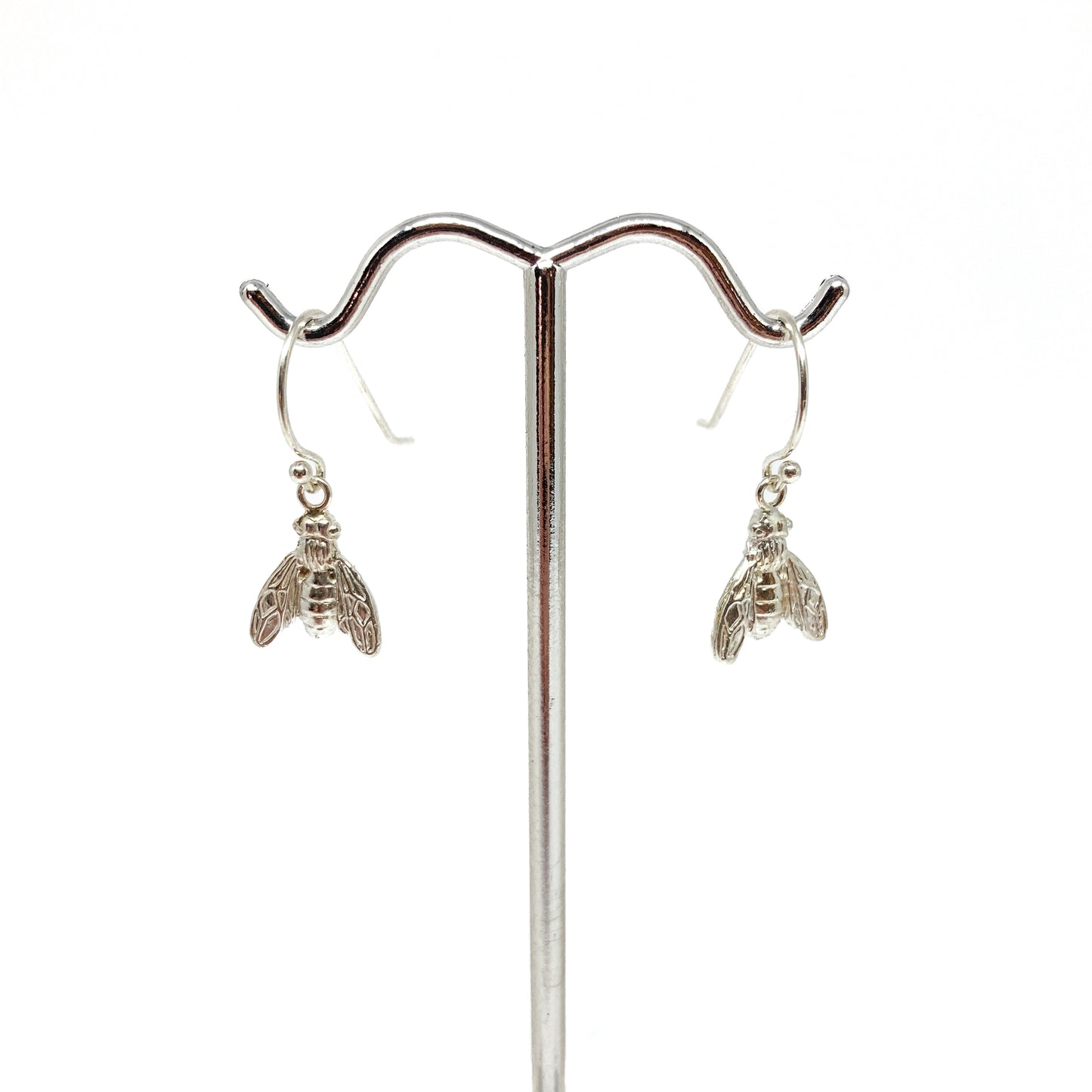 Two shiny sterling silver dangle earrings shaped like detailed bees hang from a polished metal display stand.