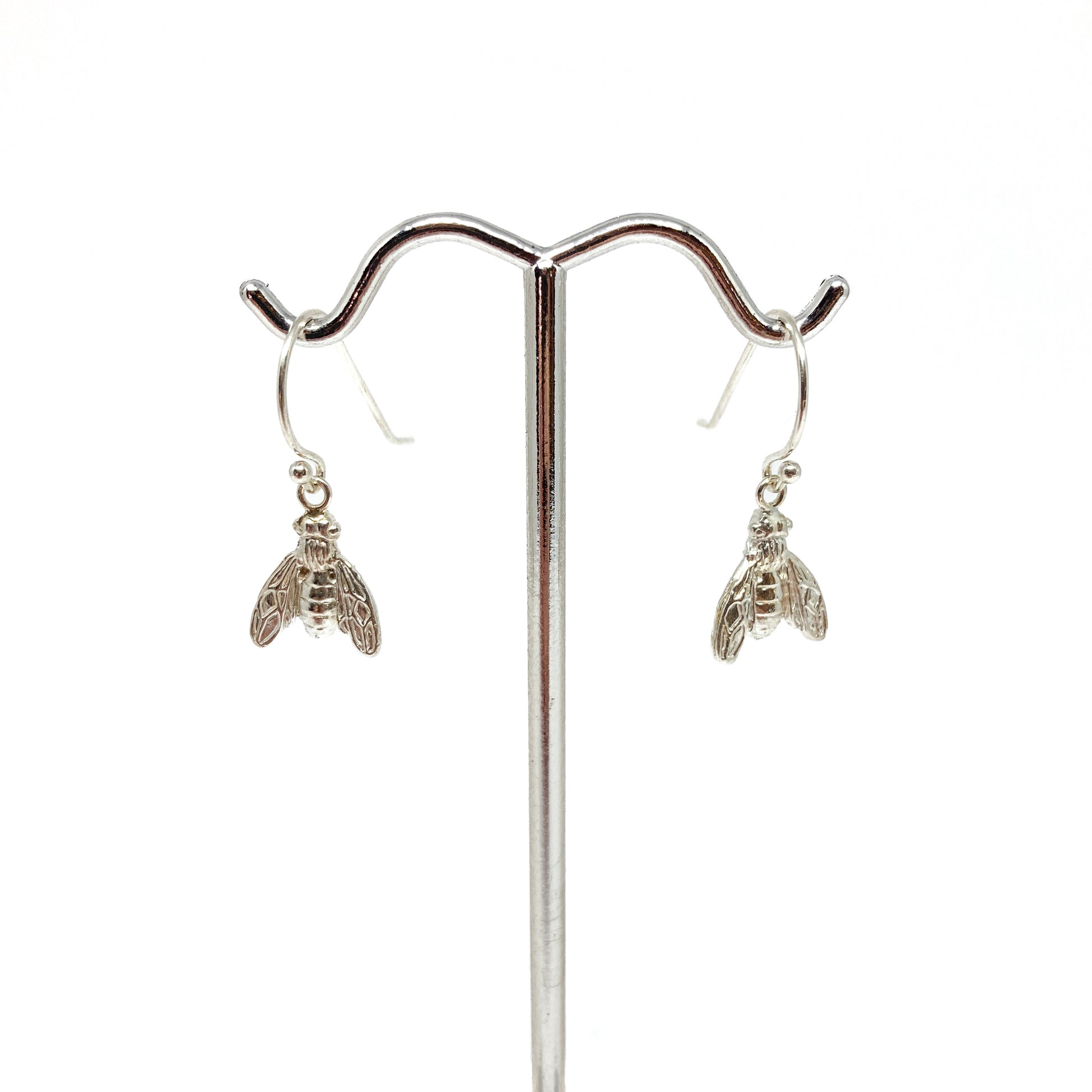 Two shiny sterling silver dangle earrings shaped like detailed bees hang from a polished metal display stand.