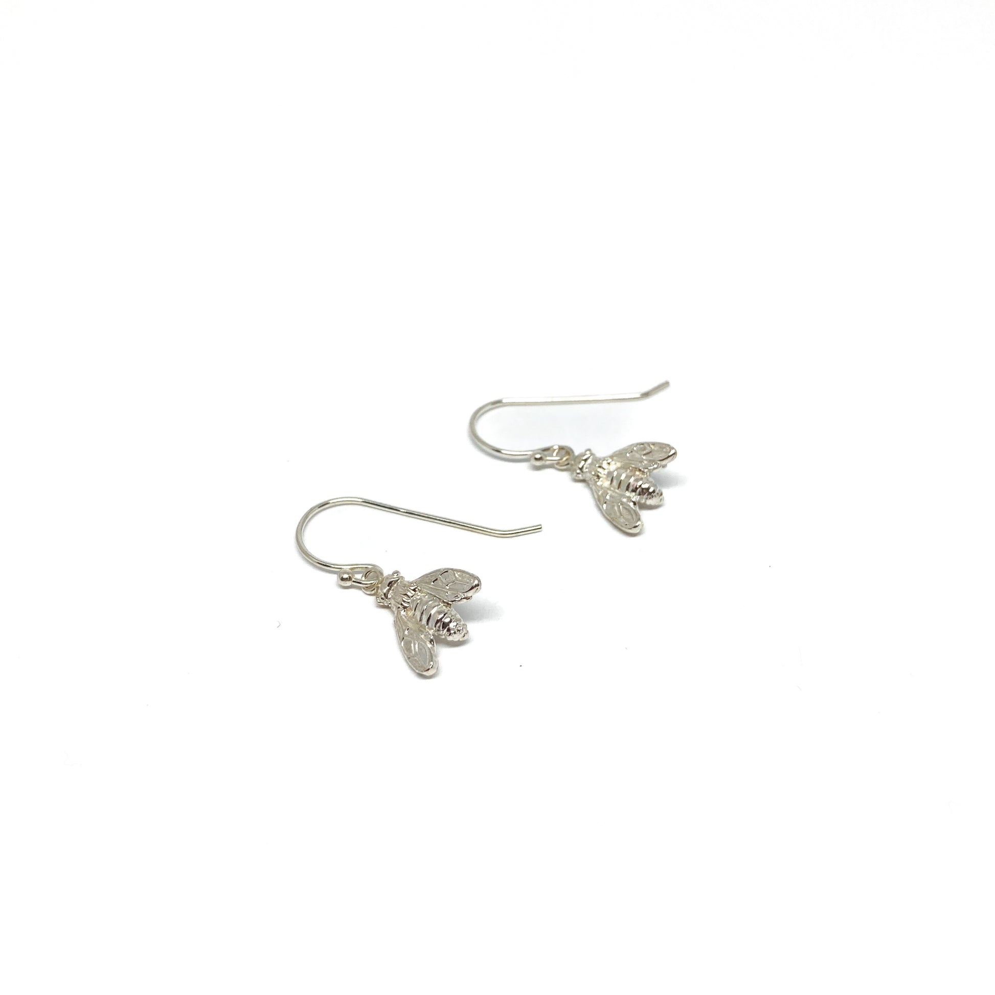 Two shiny silver dangle earrings, each shaped like a detailed bee, hang from delicate fishhook wires.