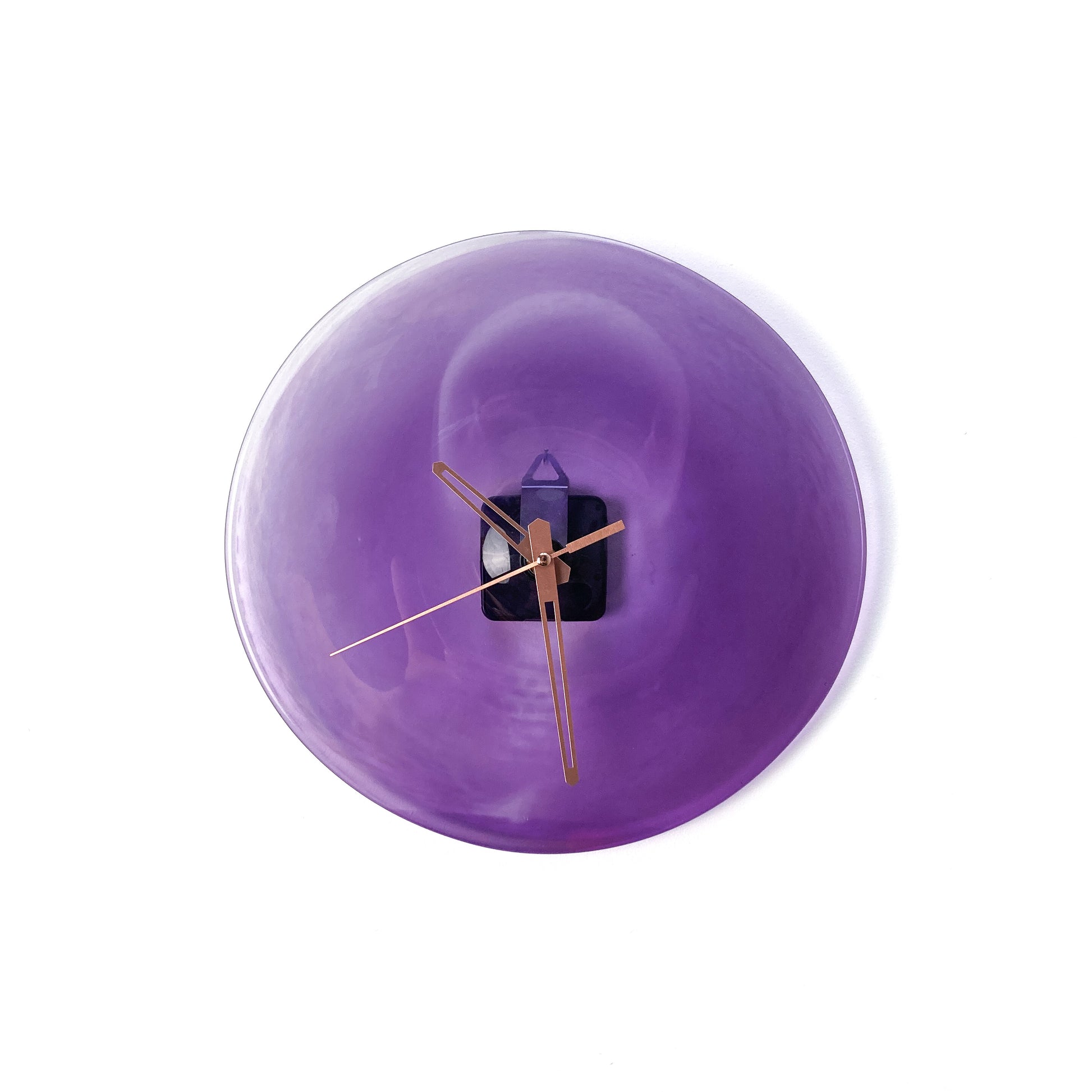 A round purple glass clock face with a lighter center, featuring thin gold-toned hour, minute, and second hands.