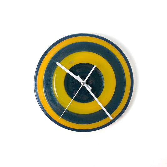 A round glass wall clock with concentric rings of yellow and blue, featuring white hands and no numerals.