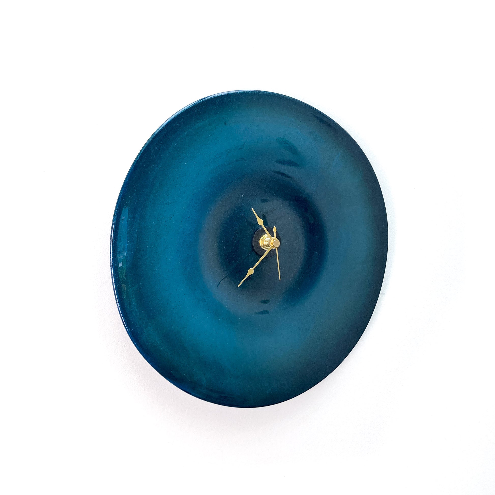 A round blue glass clock with a darker center, featuring thin gold-toned hour, minute, and second hands.