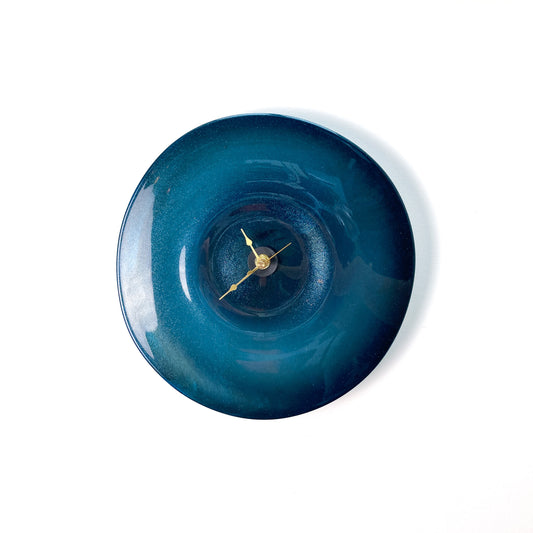 A round blue glass clock with a darker center, featuring thin gold-toned hour, minute, and second hands.