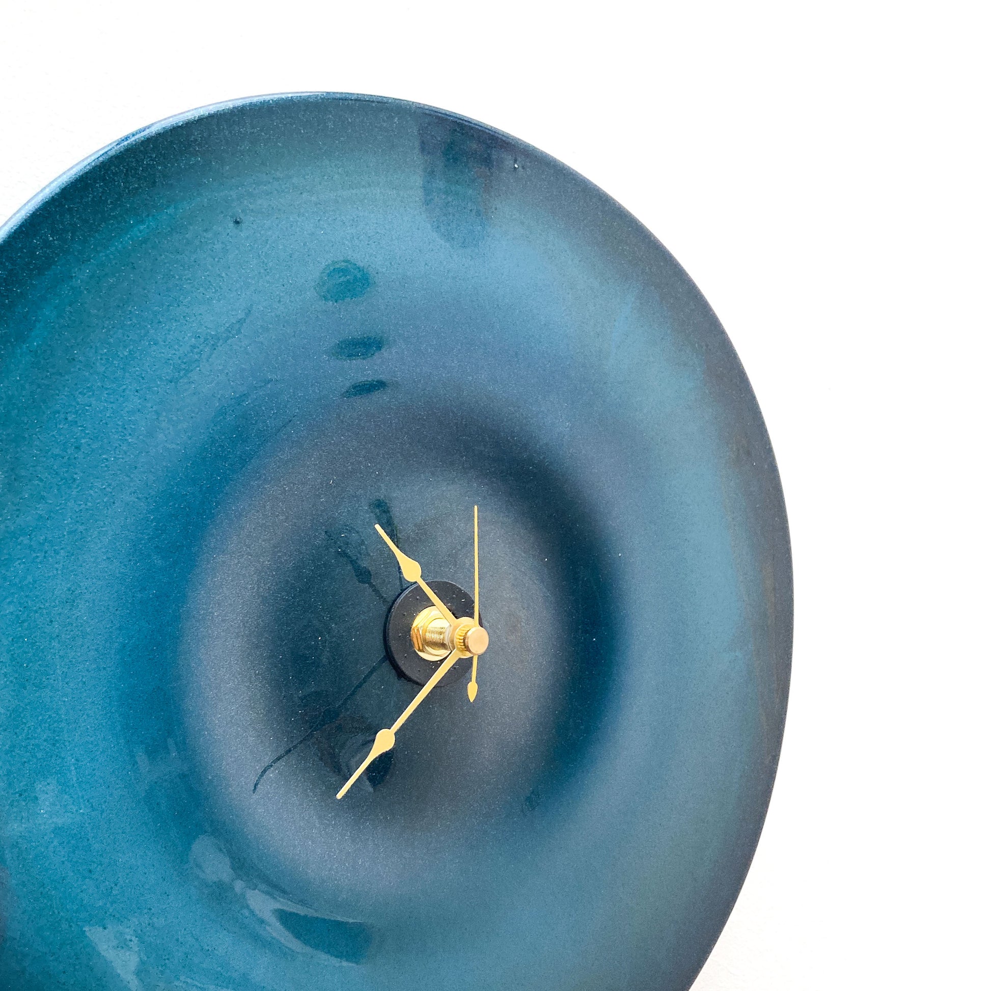 Close-up of a round, sparkly blue glass clock face with a darker center and thin gold-toned hour, minute, and second hands.