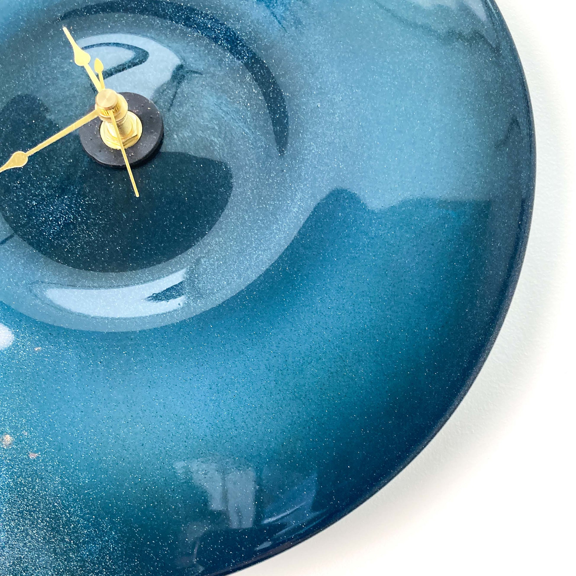 Close-up of a round, sparkly blue glass clock face with a darker center and thin gold-toned hour, minute, and second hands.
