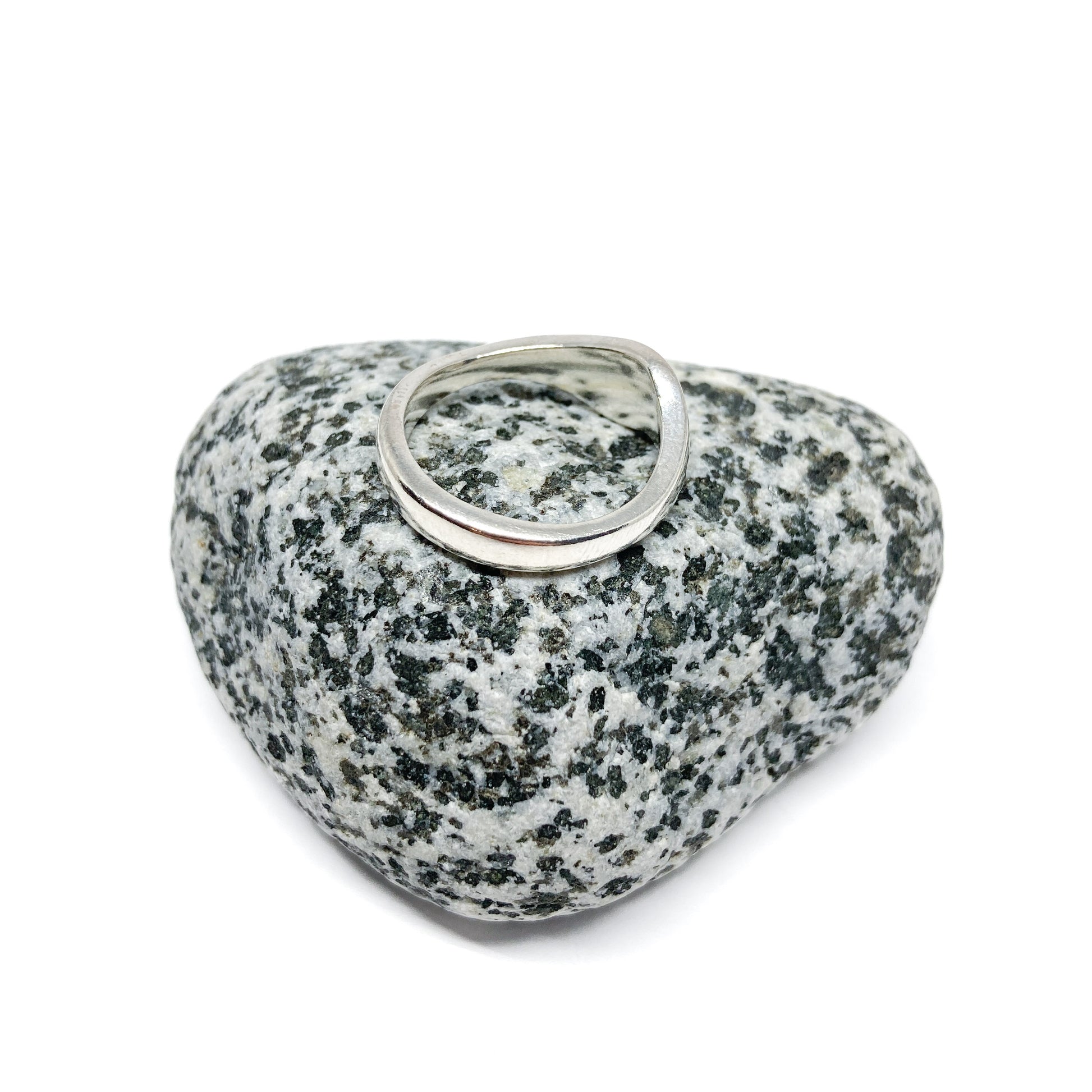 Silver wave ring on textured gray stone, close-up.