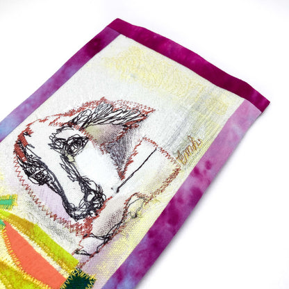 Close-up of a textile art panel showing a stylized line drawing of a dog's head and textured stitching on fabric with a dyed border.