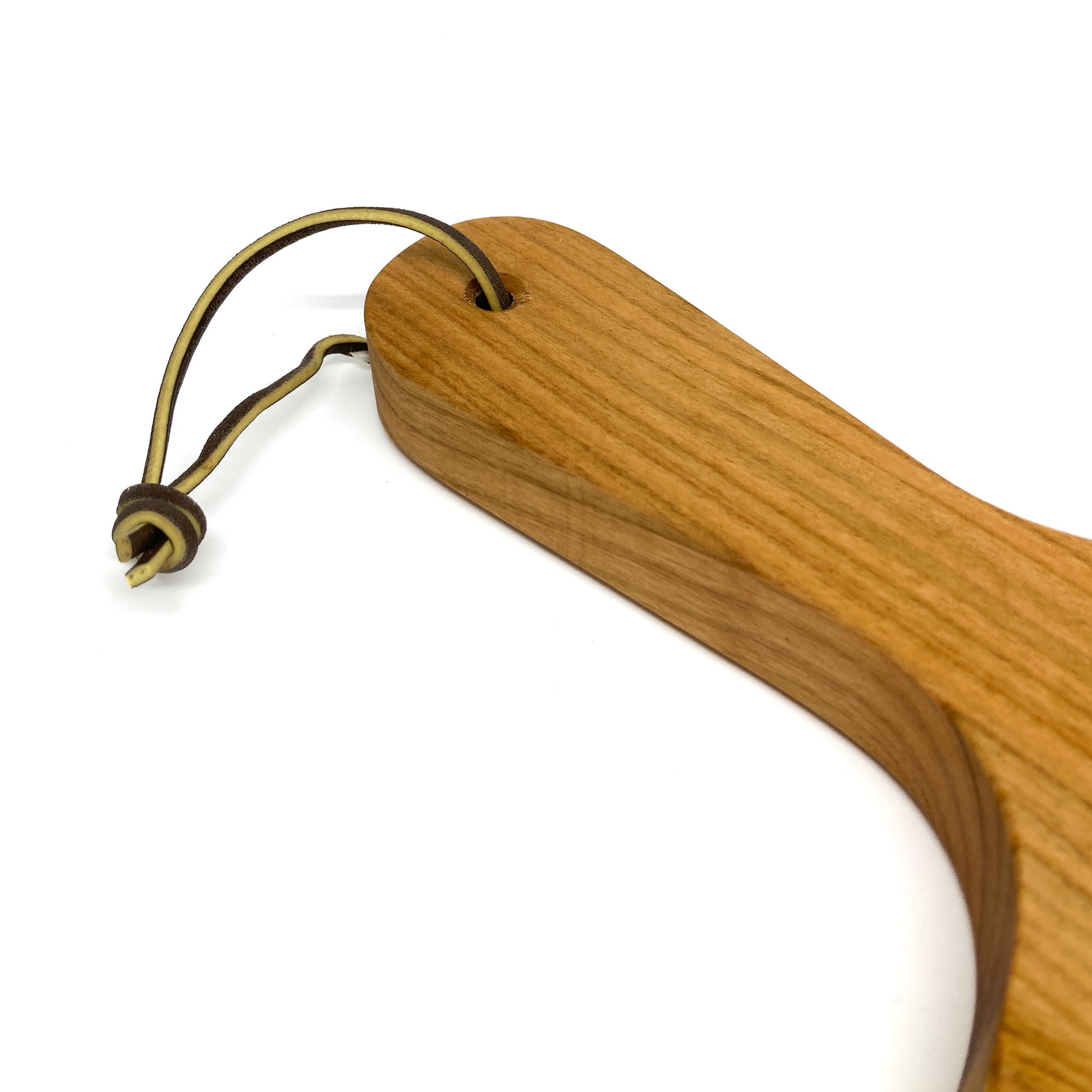 Close-up of the handle of a wooden charcuterie board, showing the hole and leather tie.