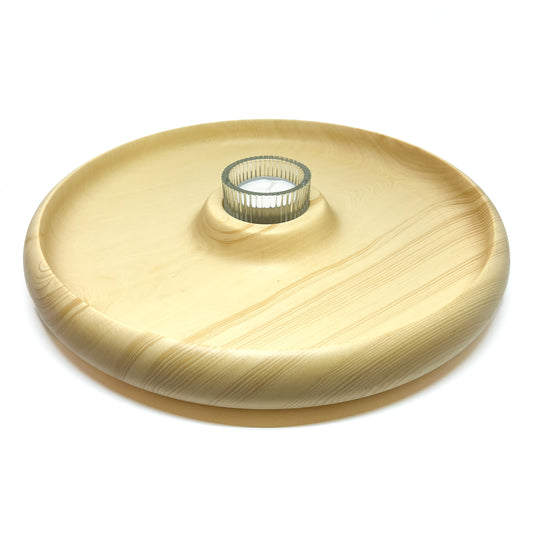 Round wooden plate with visible grain and a central elevation that surrounds a cylindrical glass container.