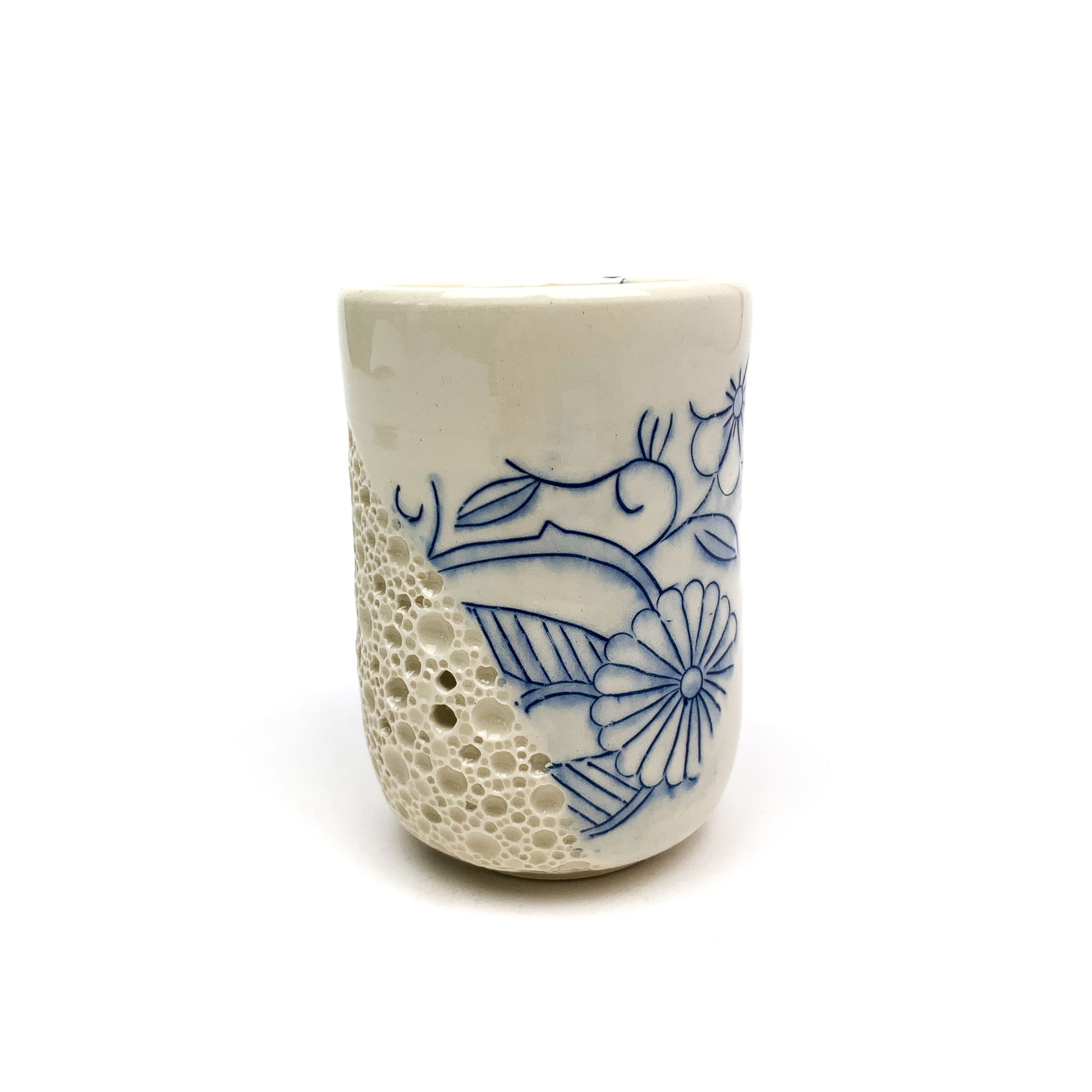 A piece of handmade pottery: a cup with a textured "bubble" design on one side and blue floral illustrations on the other.