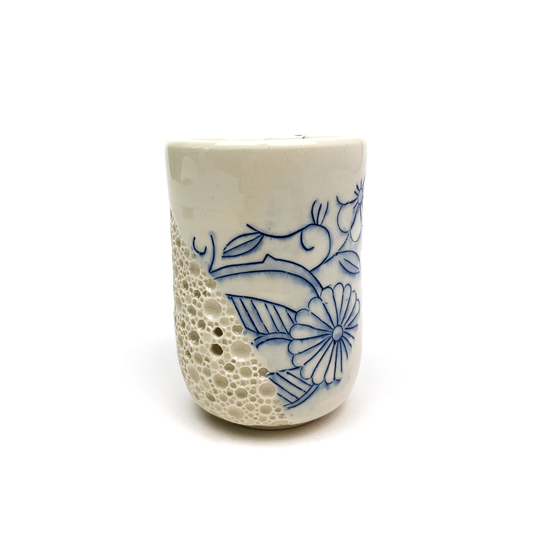 A piece of handmade pottery: a cup with a textured "bubble" design on one side and blue floral illustrations on the other.