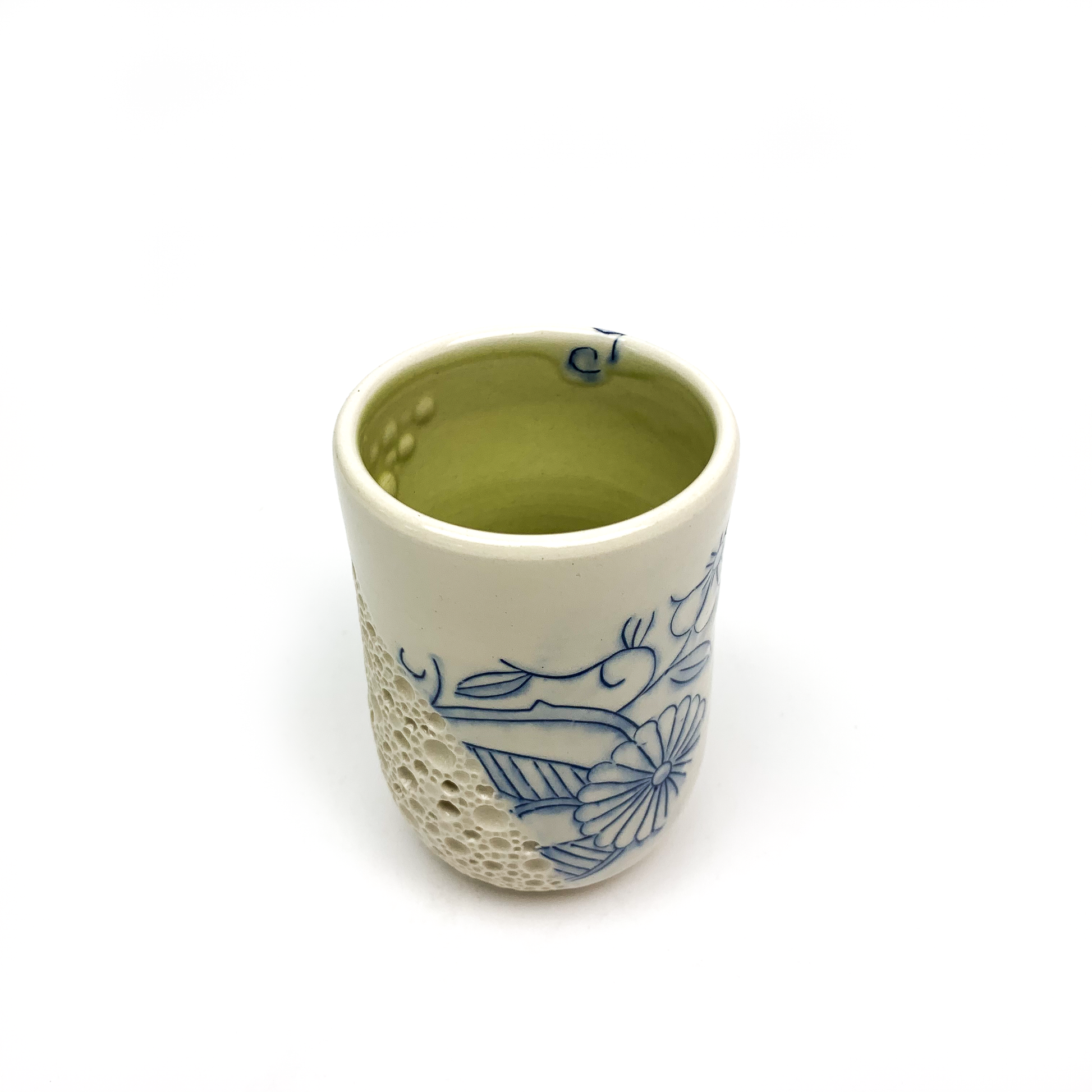 Small ceramic cup with blue floral art and a textured bubble design on its side.