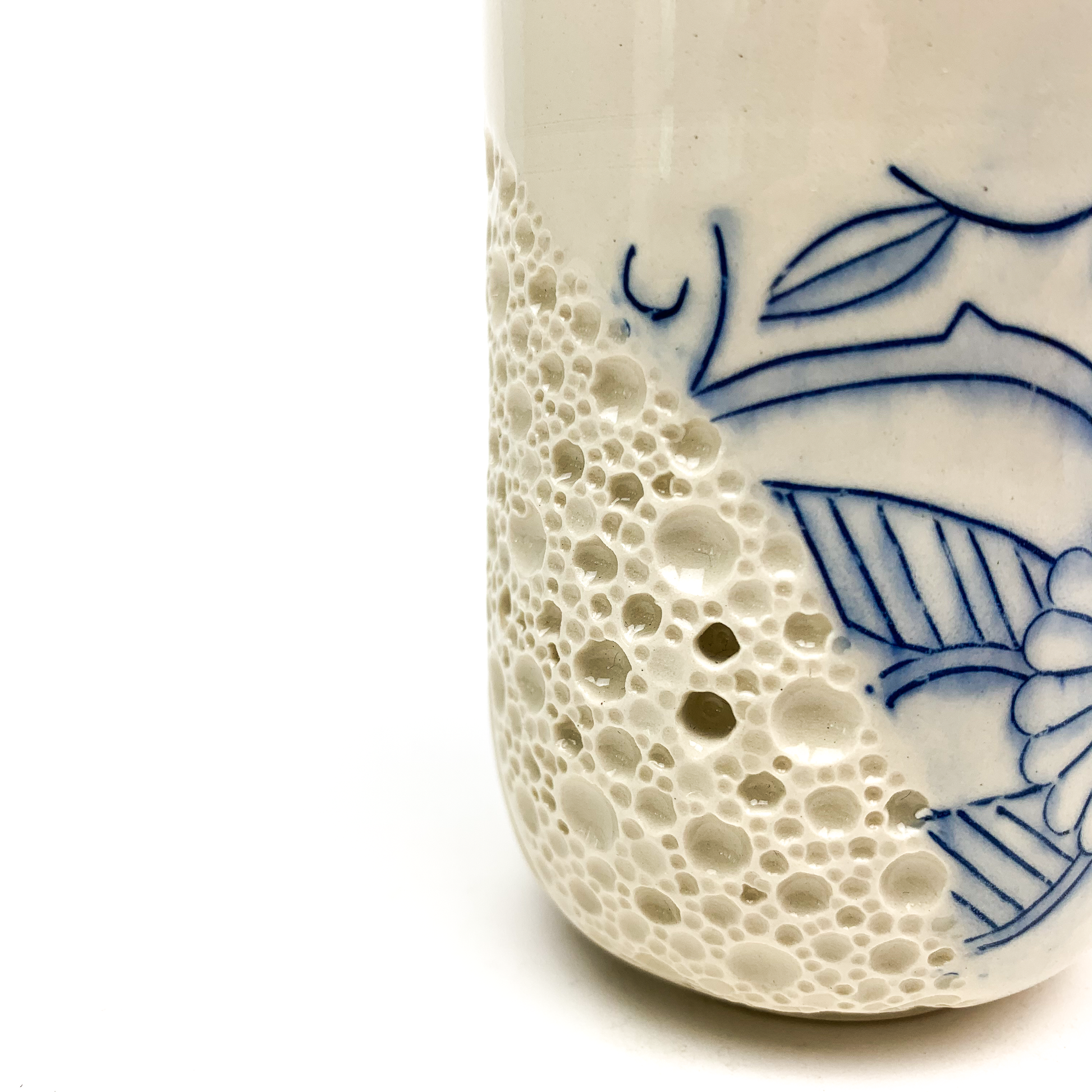 Close-up of a small ceramic cup showing blue floral art and a textured bubble pattern.