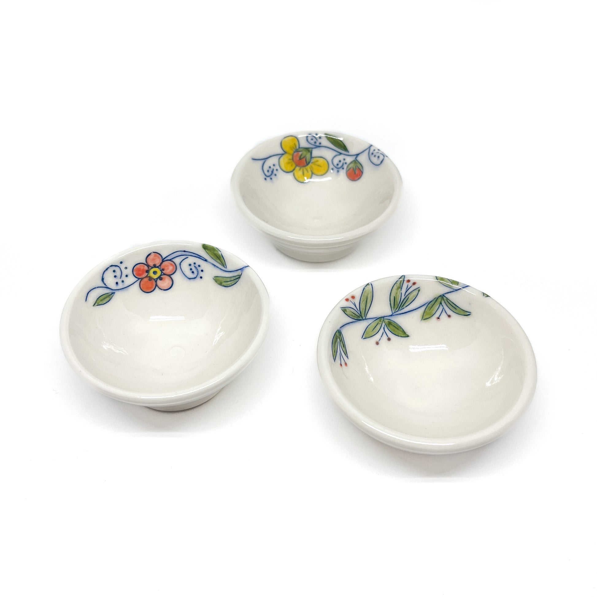 Three small handmade pottery bowls, each with a unique, colorful hand-painted floral design along the rim.
