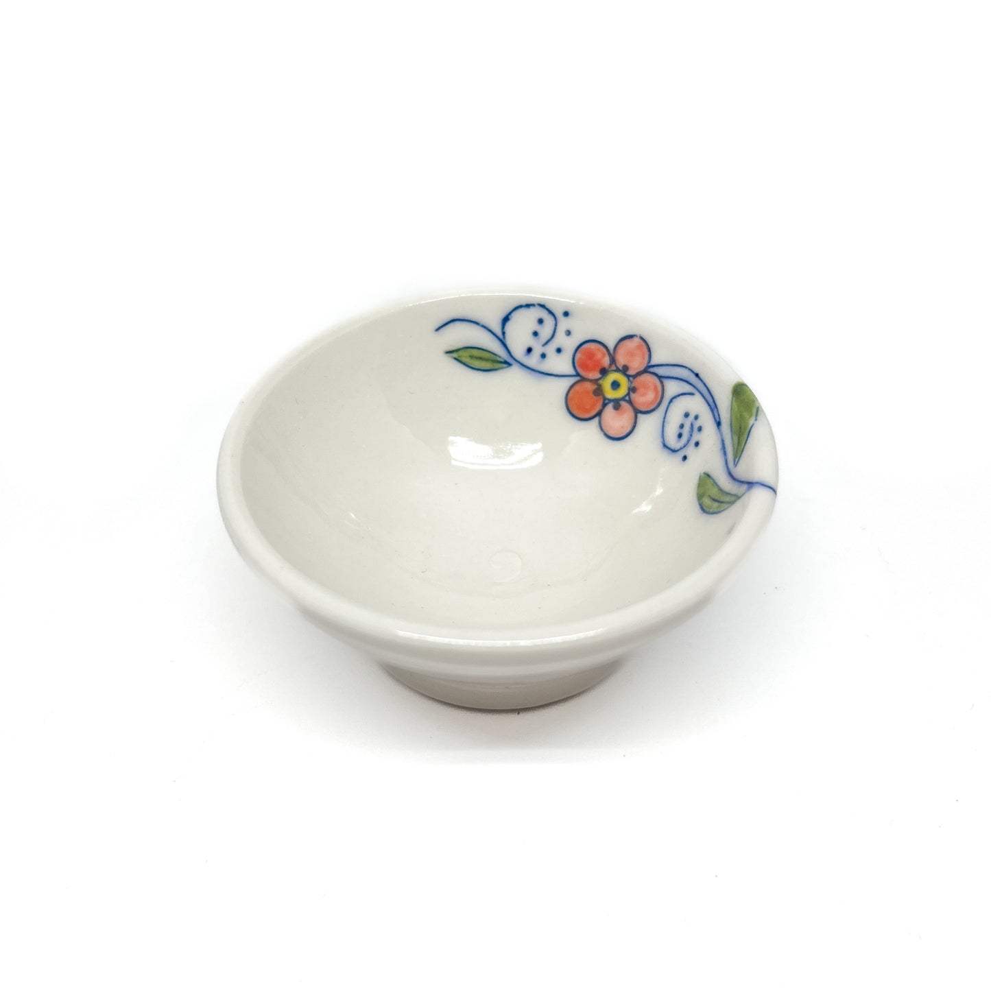 Small ceramic dish with a colorful orange flower, blue swirls, and green leaves on its rim.
