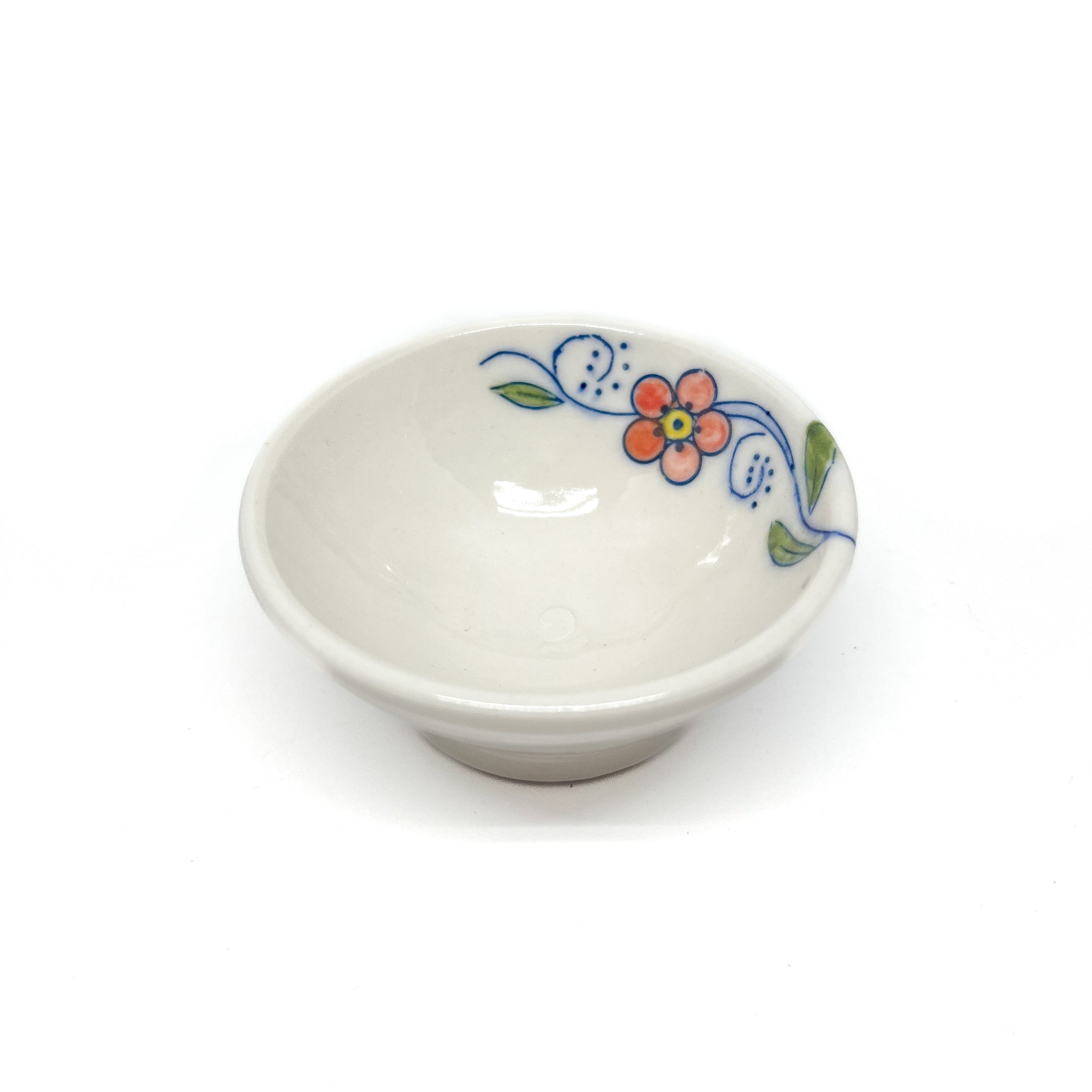 Small ceramic dish with a colorful orange flower, blue swirls, and green leaves on its rim.