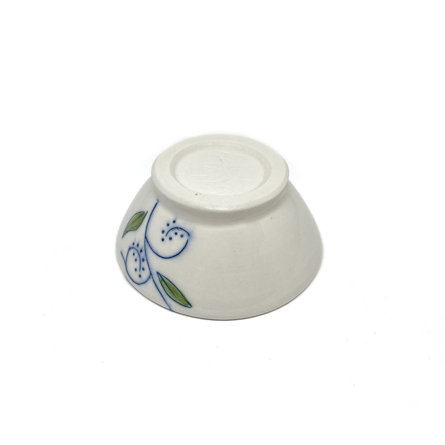 Bottom view of a small ceramic dish with blue swirls and green leaves on its side.