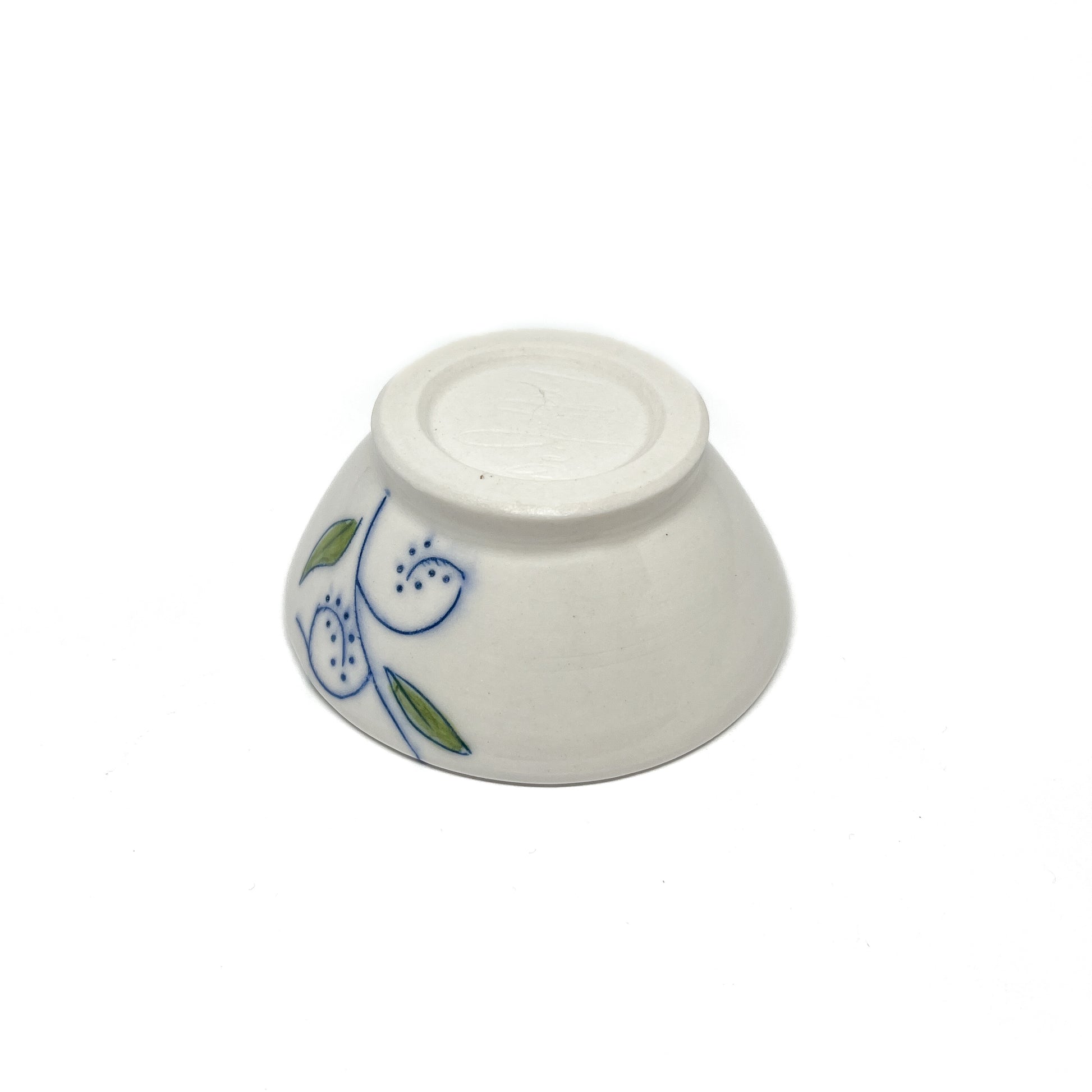 Bottom view of a small ceramic dish with blue swirls and green leaves on its side.