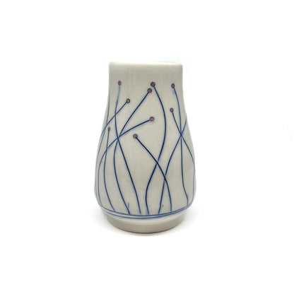 A piece of handmade pottery: a small vase with delicate blue line art and small red dots on a light base.