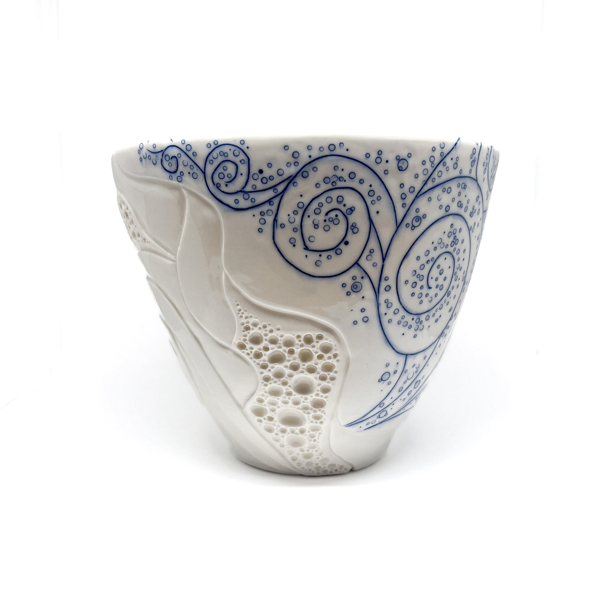 Handmade pottery bowl featuring carved white abstract forms and detailed blue swirling lines with dot accents.