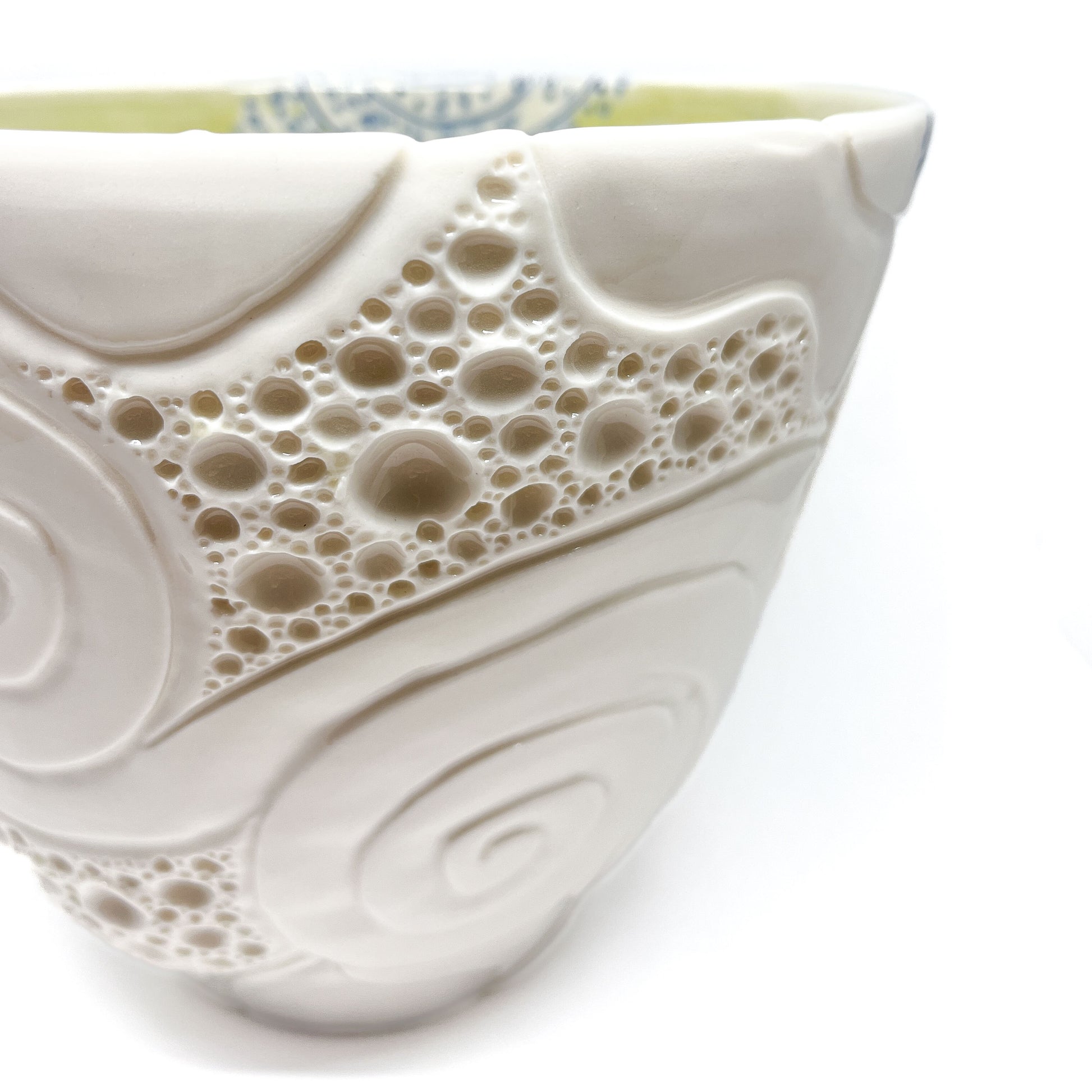 Close-up of a ceramic bowl with textured swirl and bubble patterns and a blue patterned rim.