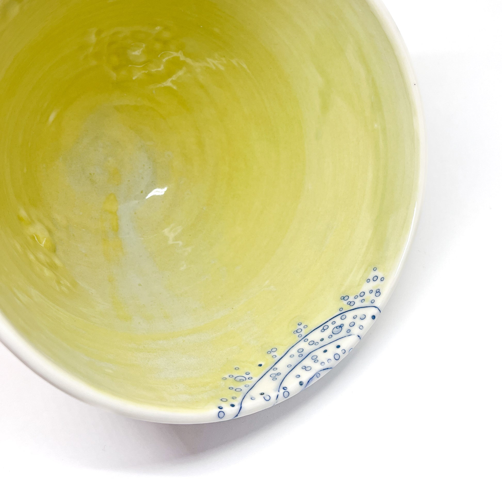 Partial top view of a ceramic bowl with a smooth interior and blue abstract designs along the edge.