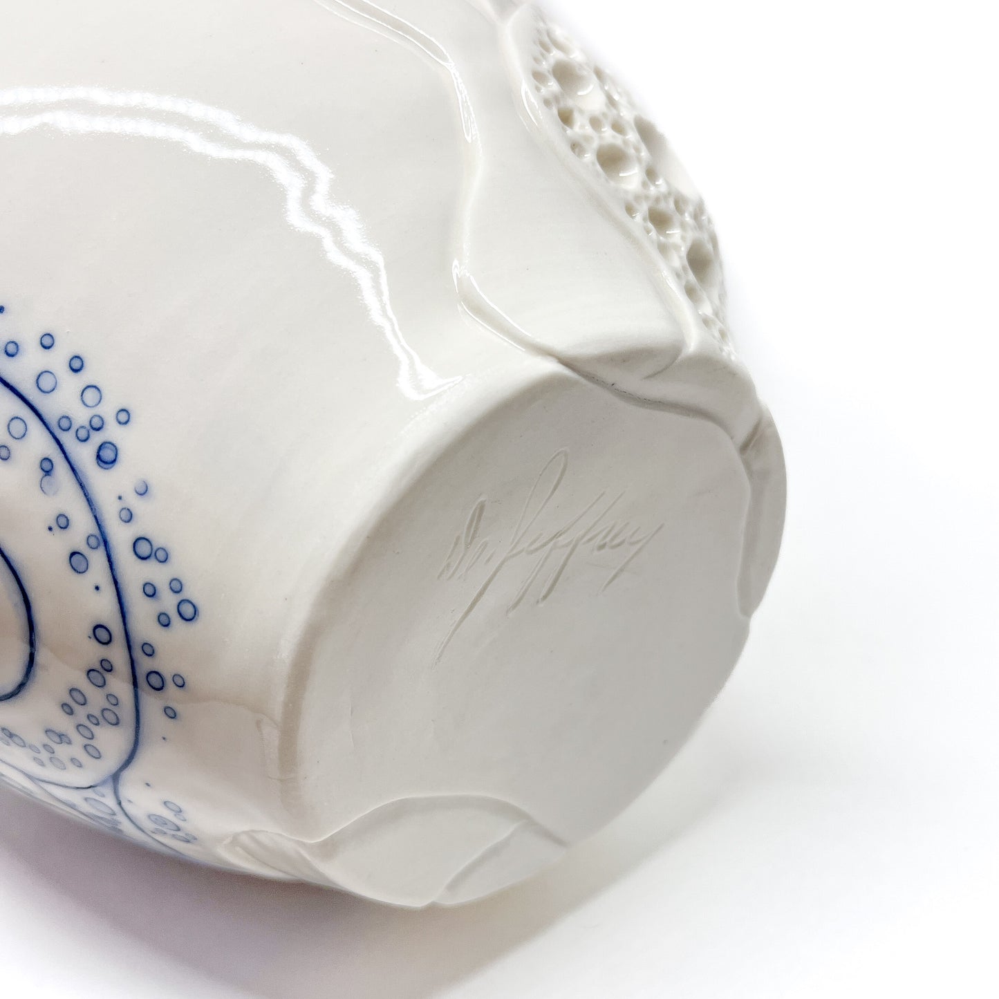 Bottom of a small ceramic bowl with blue abstract dots and lines, textured areas, and a signature.