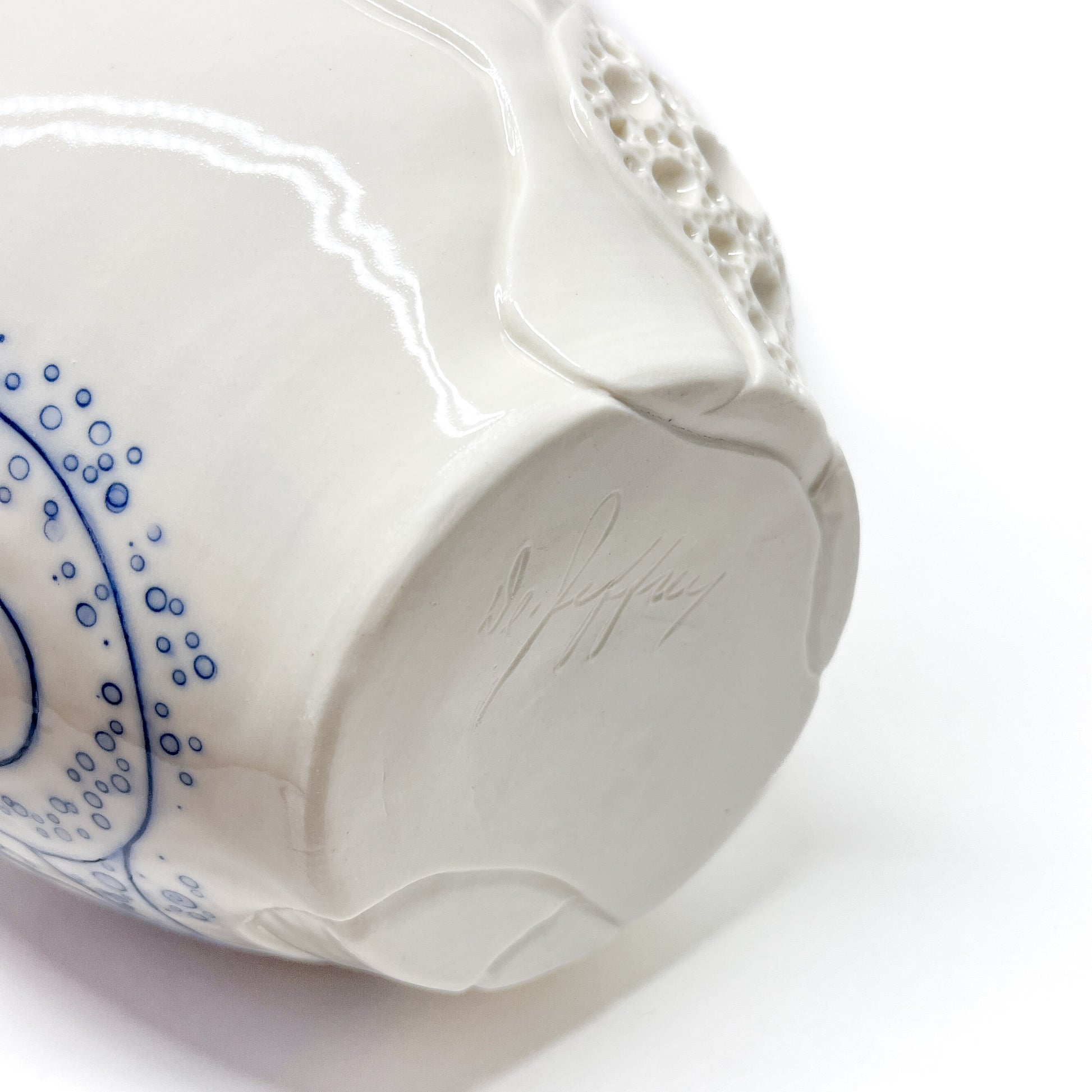Bottom of a small ceramic bowl with blue abstract dots and lines, textured areas, and a signature.