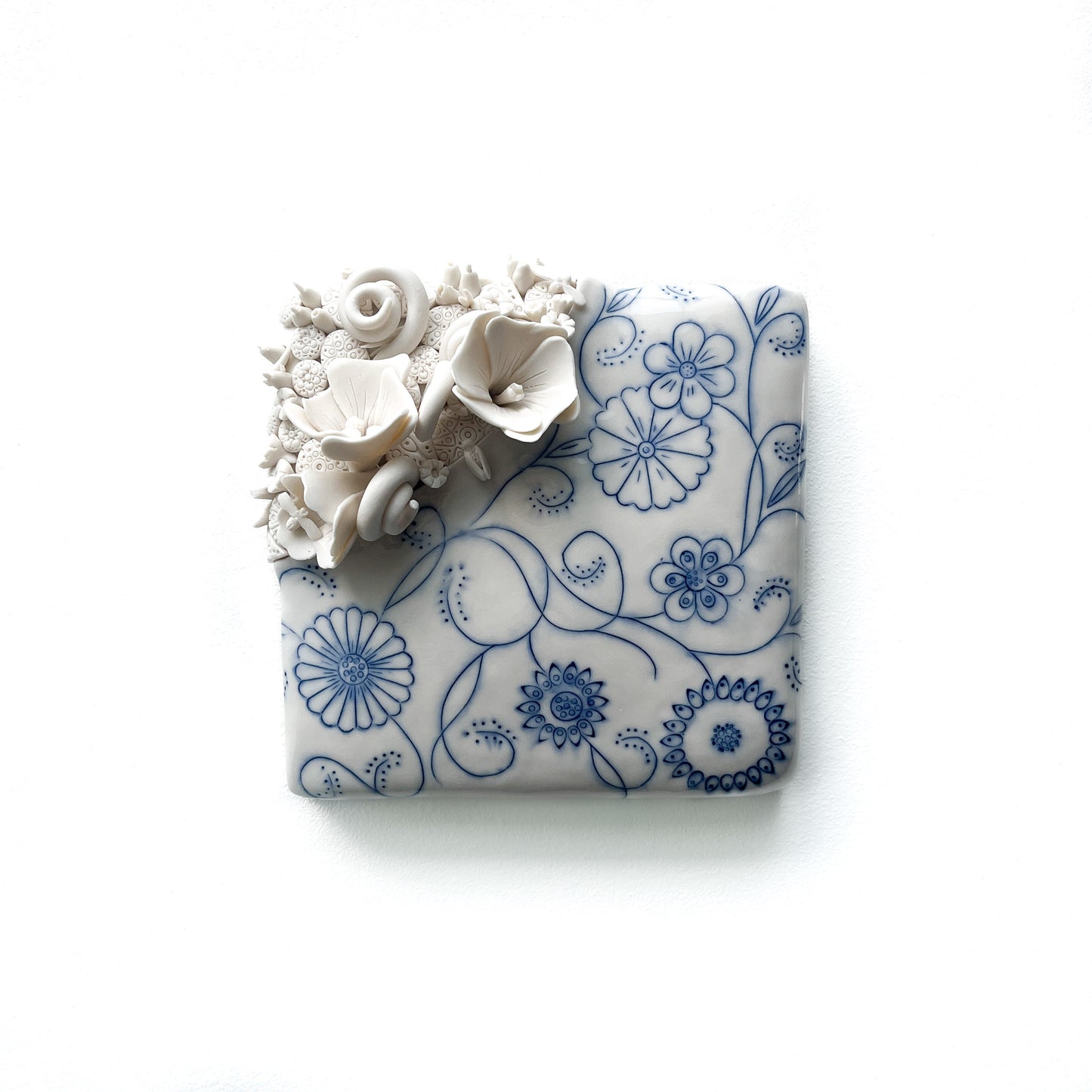 Handmade pottery tile with raised white floral sculptures and delicate blue floral line art.