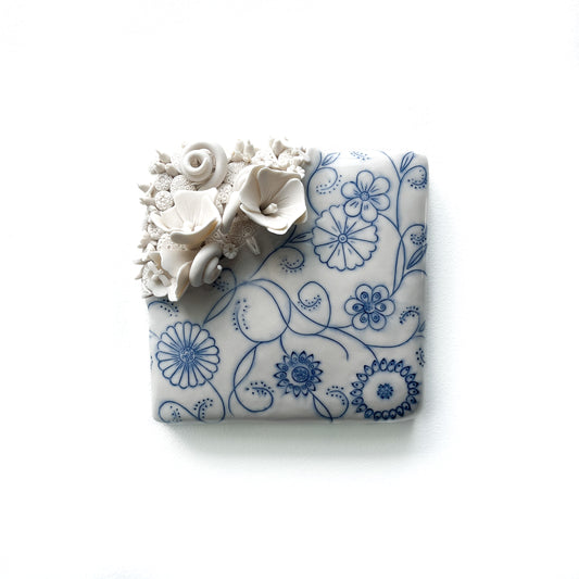 Handmade pottery tile with raised white floral sculptures and delicate blue floral line art.