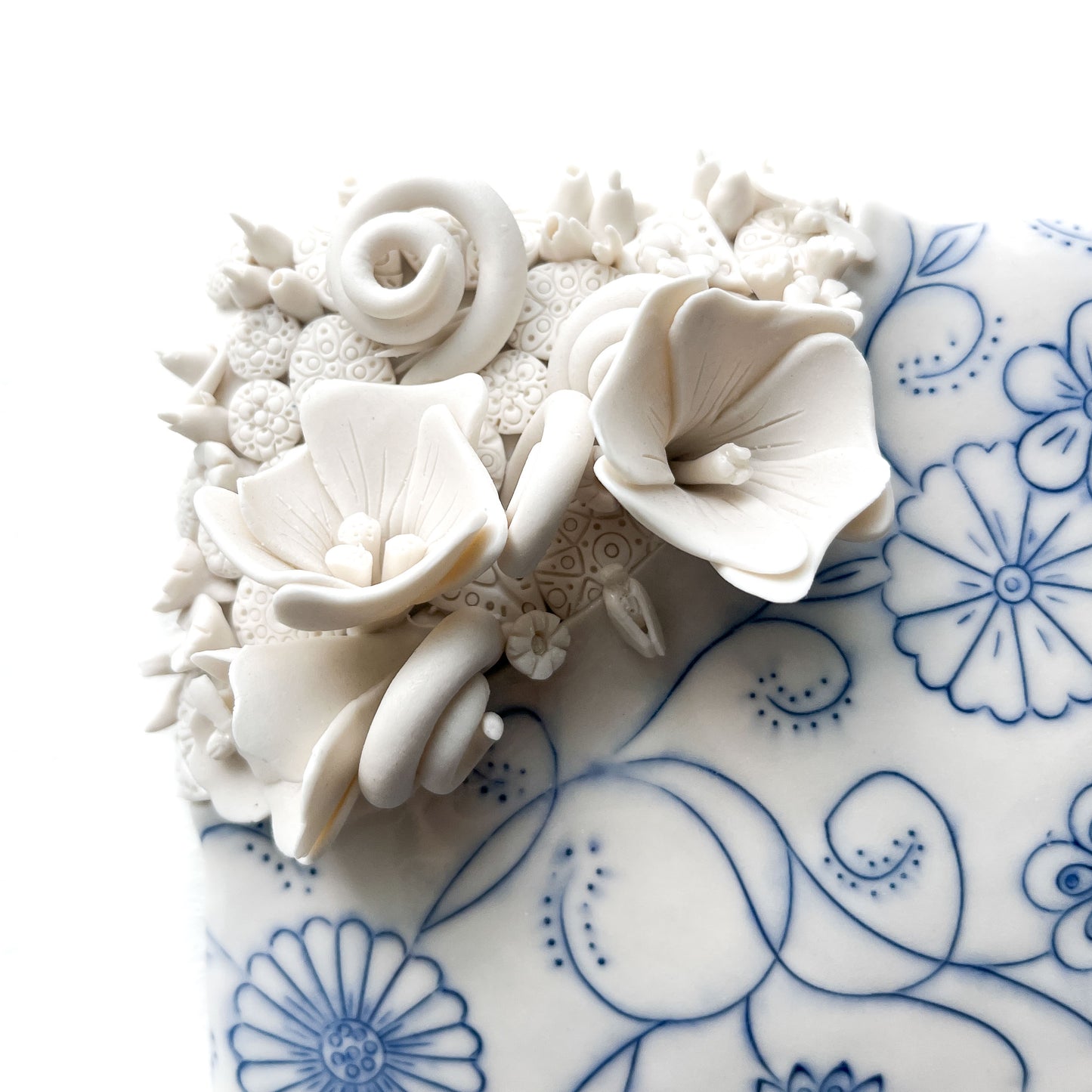 Close-up of a ceramic tile with blue floral designs and raised, textured white flowers and buds.