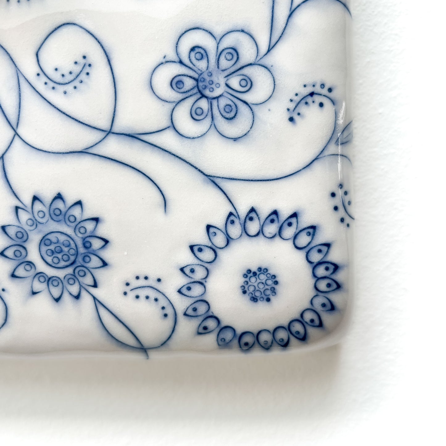 Corner close-up of a ceramic tile with intricate blue floral line art details.