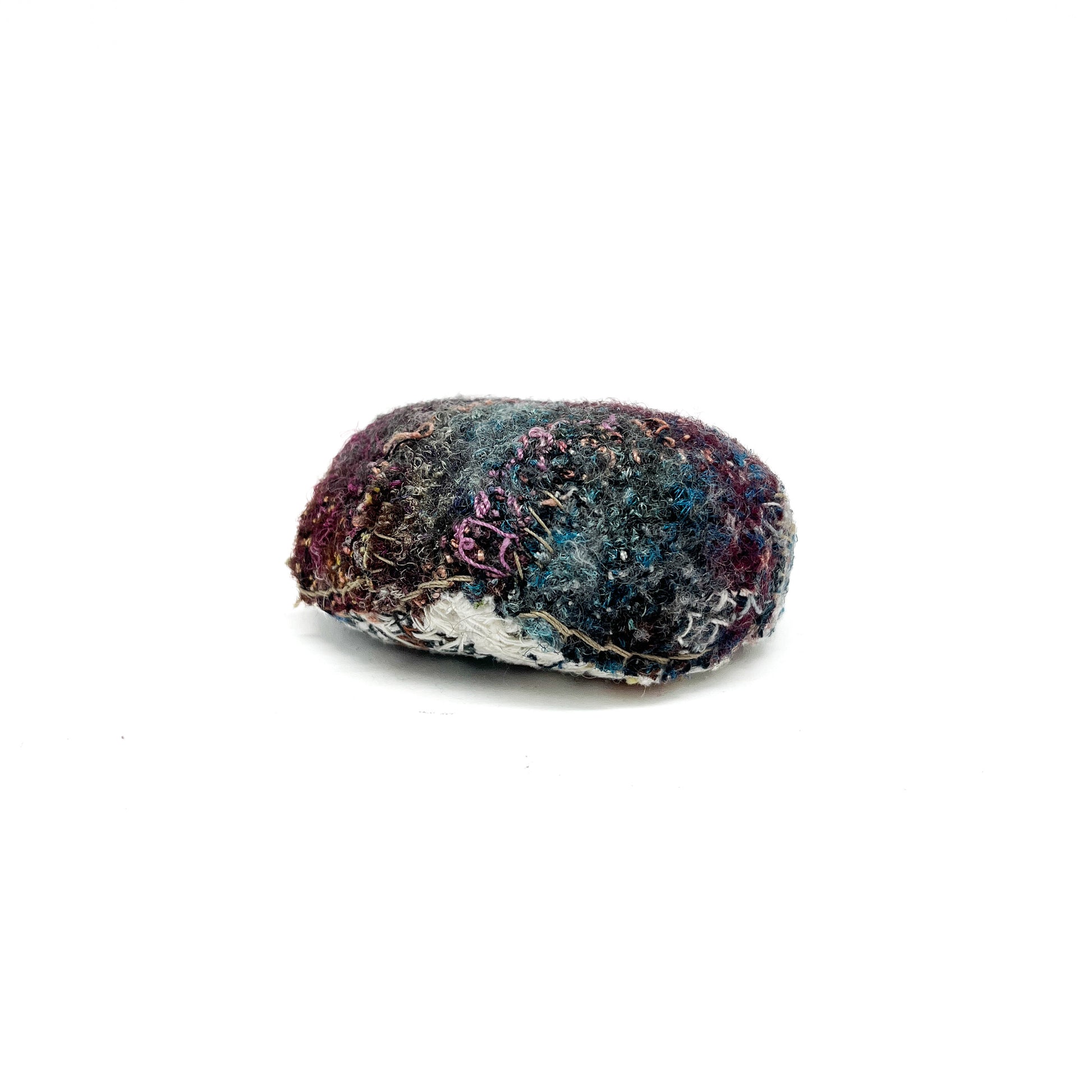 Embroidered Rock by Jane Kenyon: Oval textured textile art resembling a rock, with layered stitching in purple, blue, white, and gold threads.