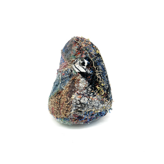 A uniquely shaped rock adorned with rich, colorful textile embroidery.