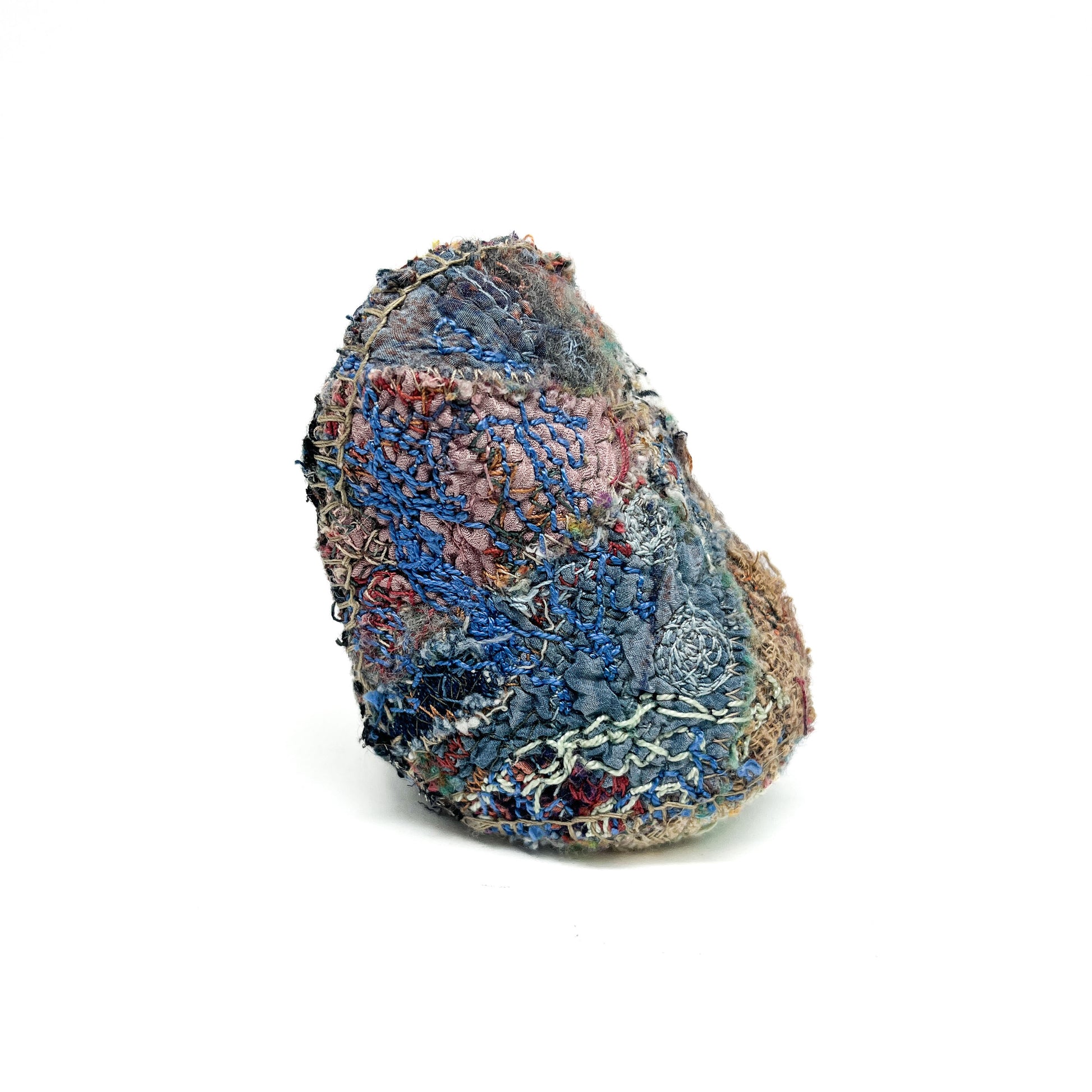 A textured, rounded object covered in layers of colorful, stitched fabric and threads.