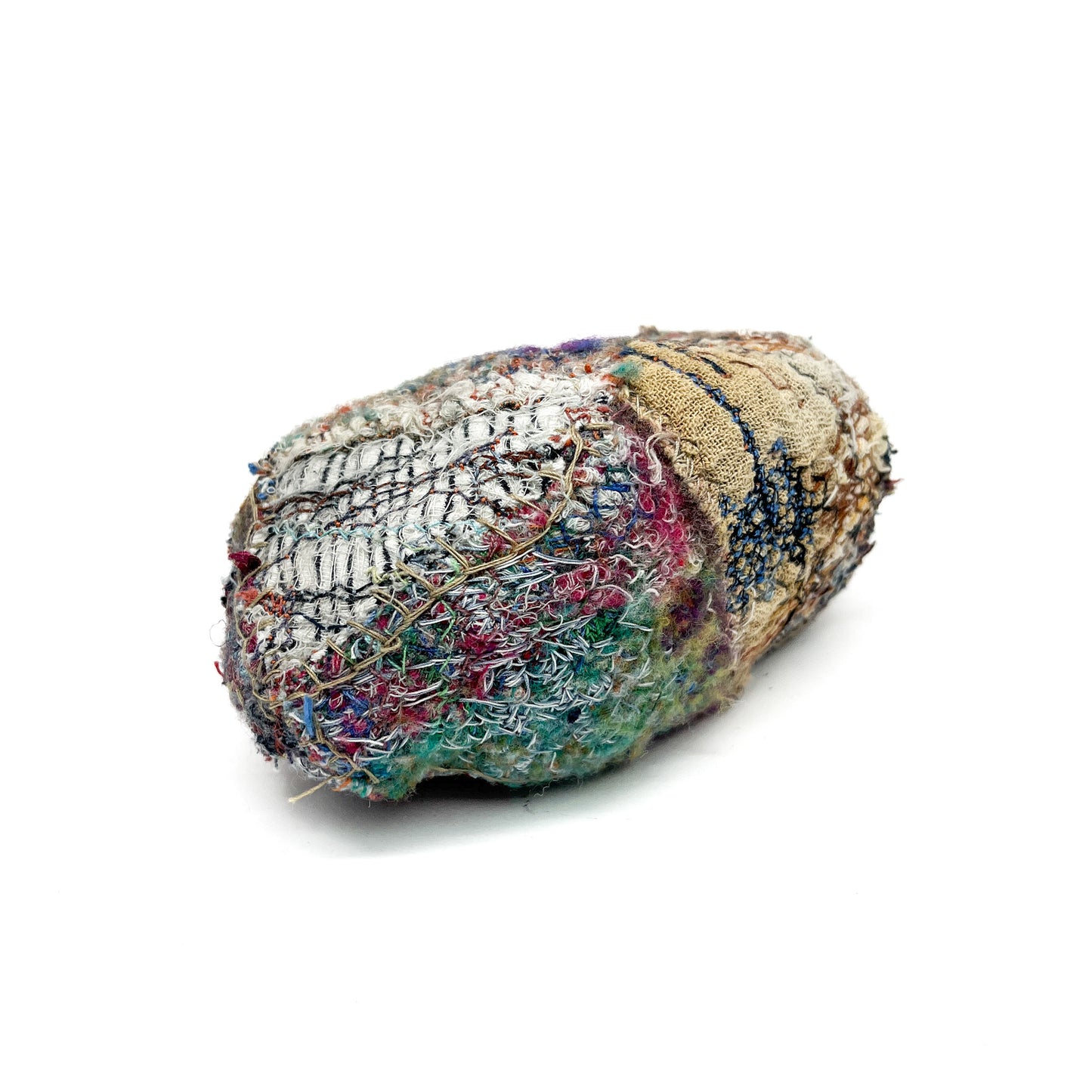 Oblong textile sculpture with a dense, textured surface of colorful threads and stitching.