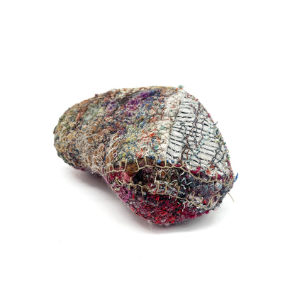 Heavily textured, rounded textile object with layers of colorful stitching and varied fabric