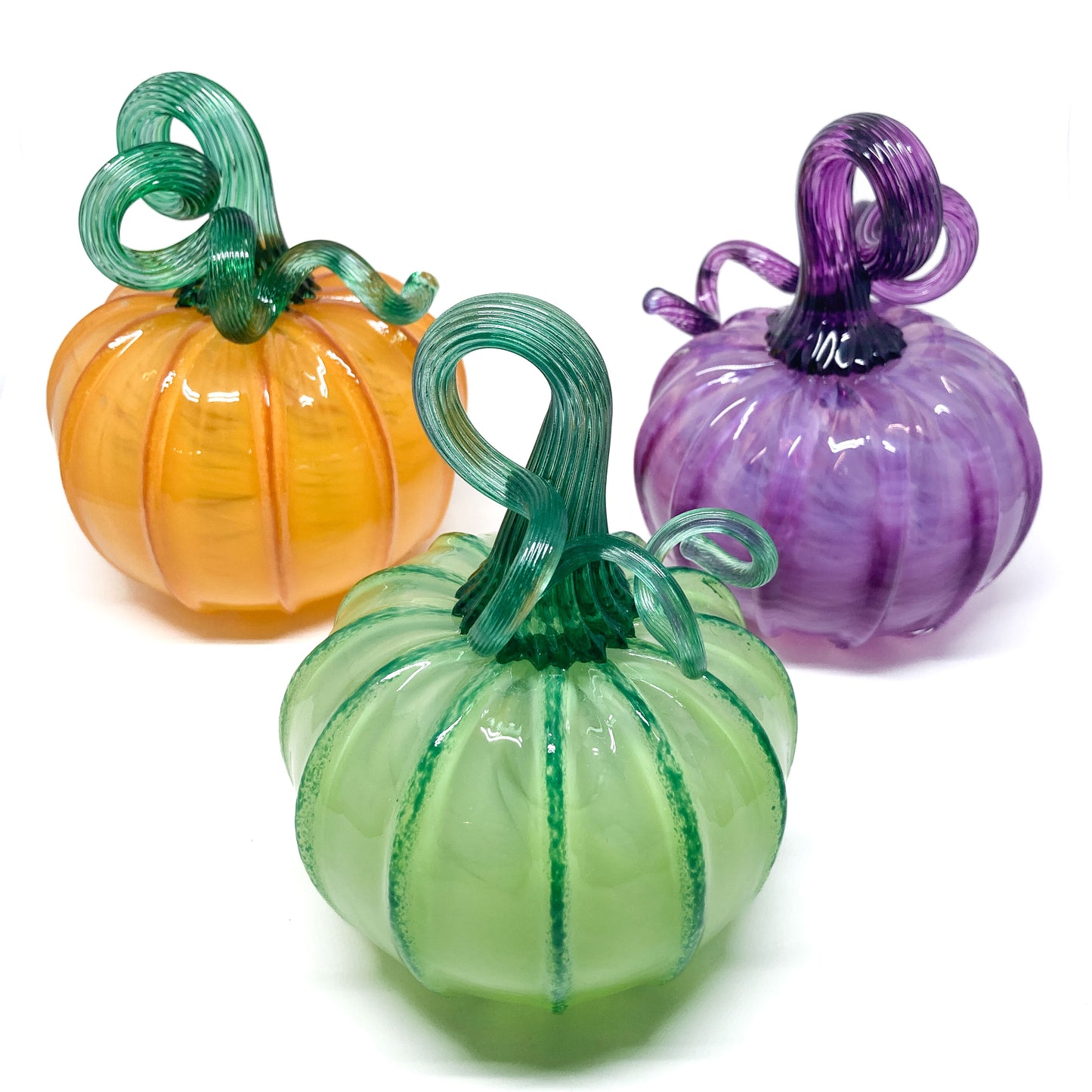 Three glass pumpkins in orange, green, and purple, each with a curled, matching glass stem.