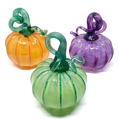 Three glass pumpkins in orange, green, and purple, each with a curled, matching glass stem.