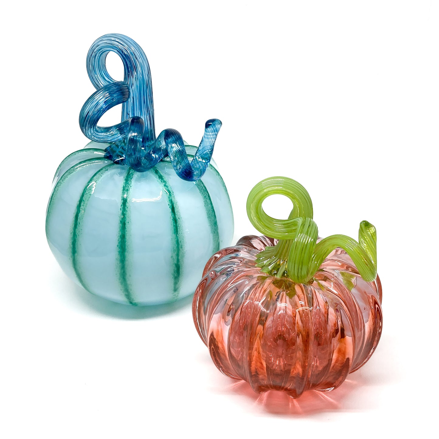 Two glass pumpkins, one light blue with a blue stem and one pink with a green stem.