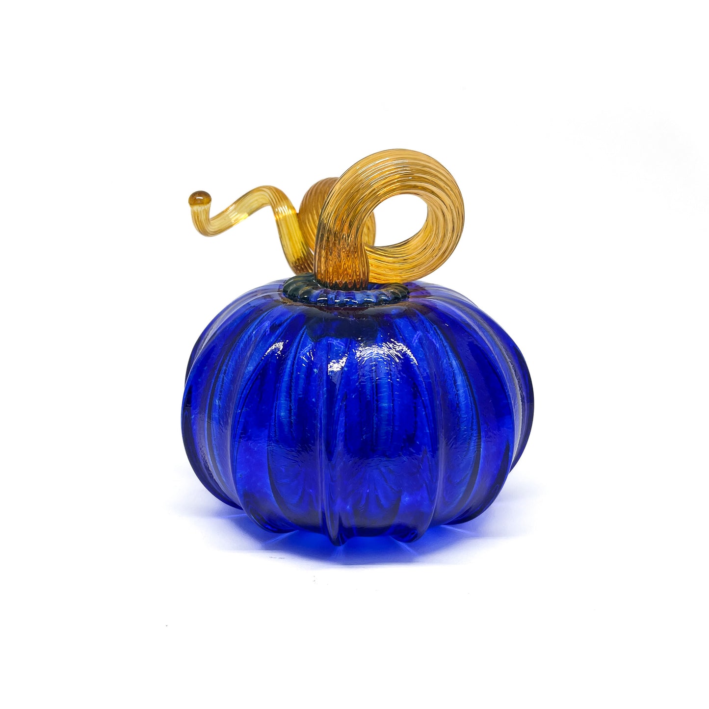 A cobalt blue glass pumpkin with a curled, amber-colored stem.