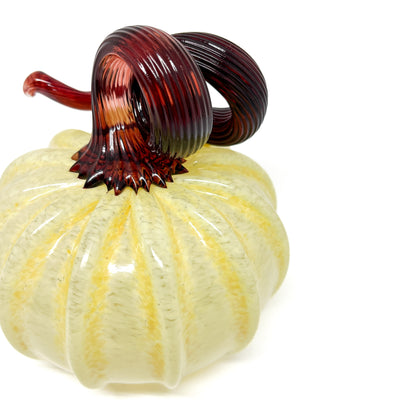 A pale yellow glass pumpkin with a curled, dark red glass stem.