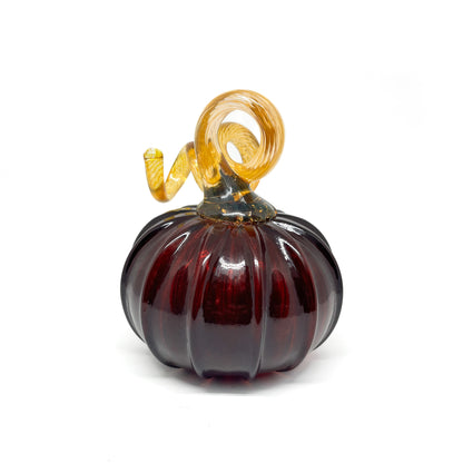 A dark red glass pumpkin with a curled, amber-colored stem.