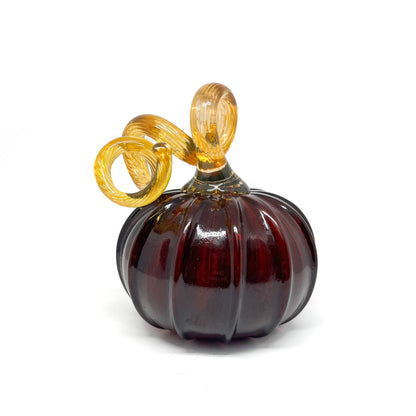 A dark red glass pumpkin with a curled, amber-colored stem.
