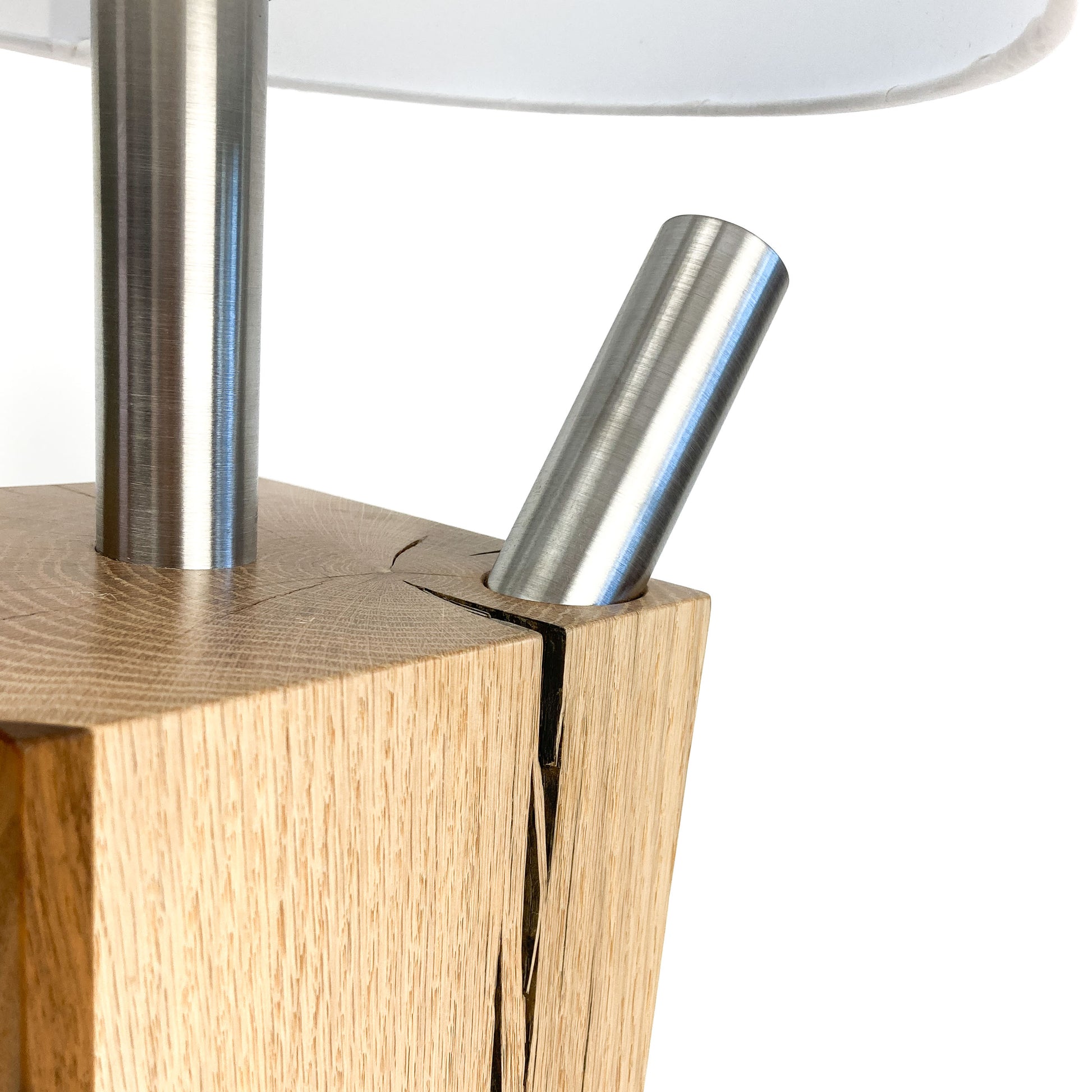 Close-up of a lamp base: light wood block with two metal rods, one vertical, one angled.