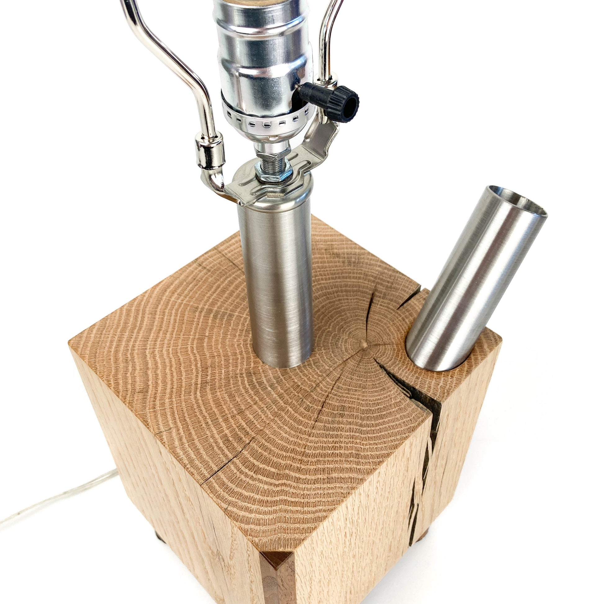 Top-down view of a lamp base: light wood block, two metal rods.