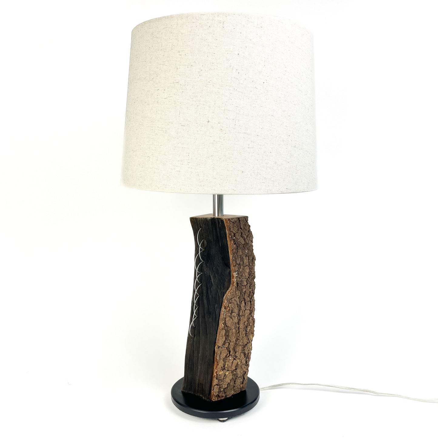 A table lamp with a textured wood base, white shade, and black round base.