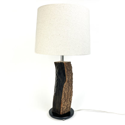 A table lamp with a textured wood base, white shade, and black round base.