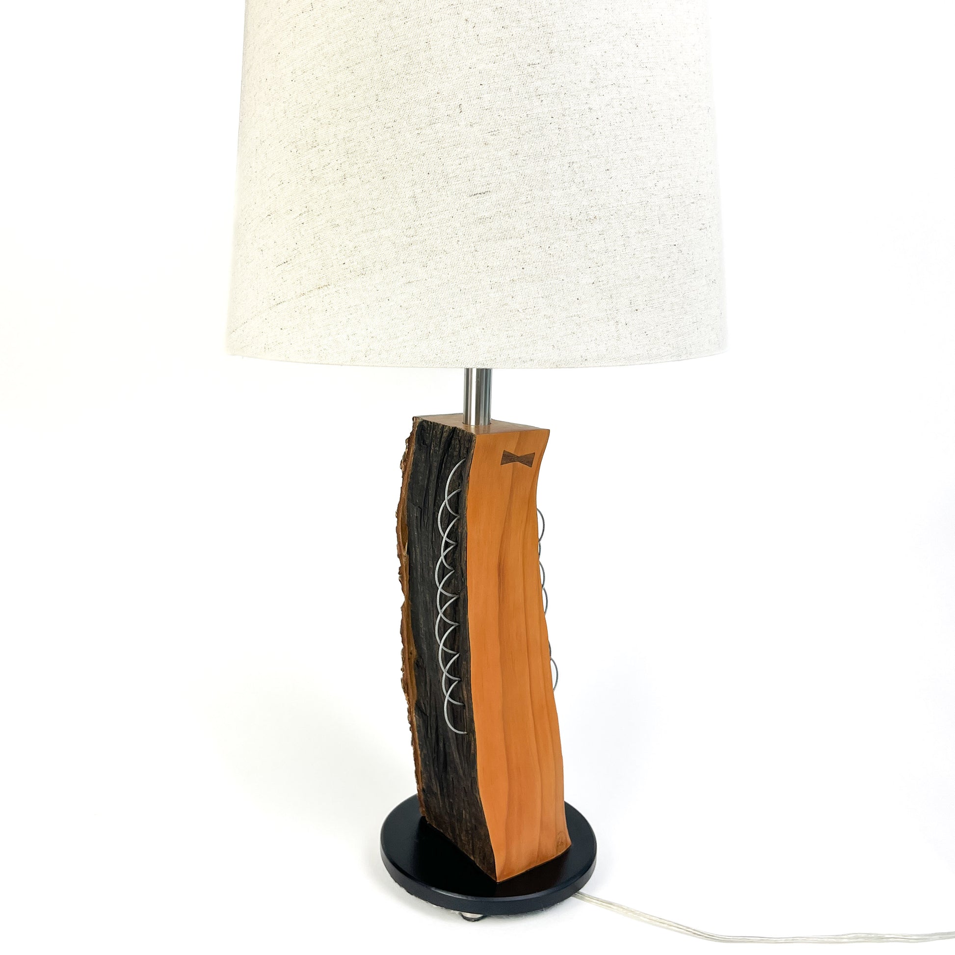 A table lamp with a textured wood base, white shade, and black round base.