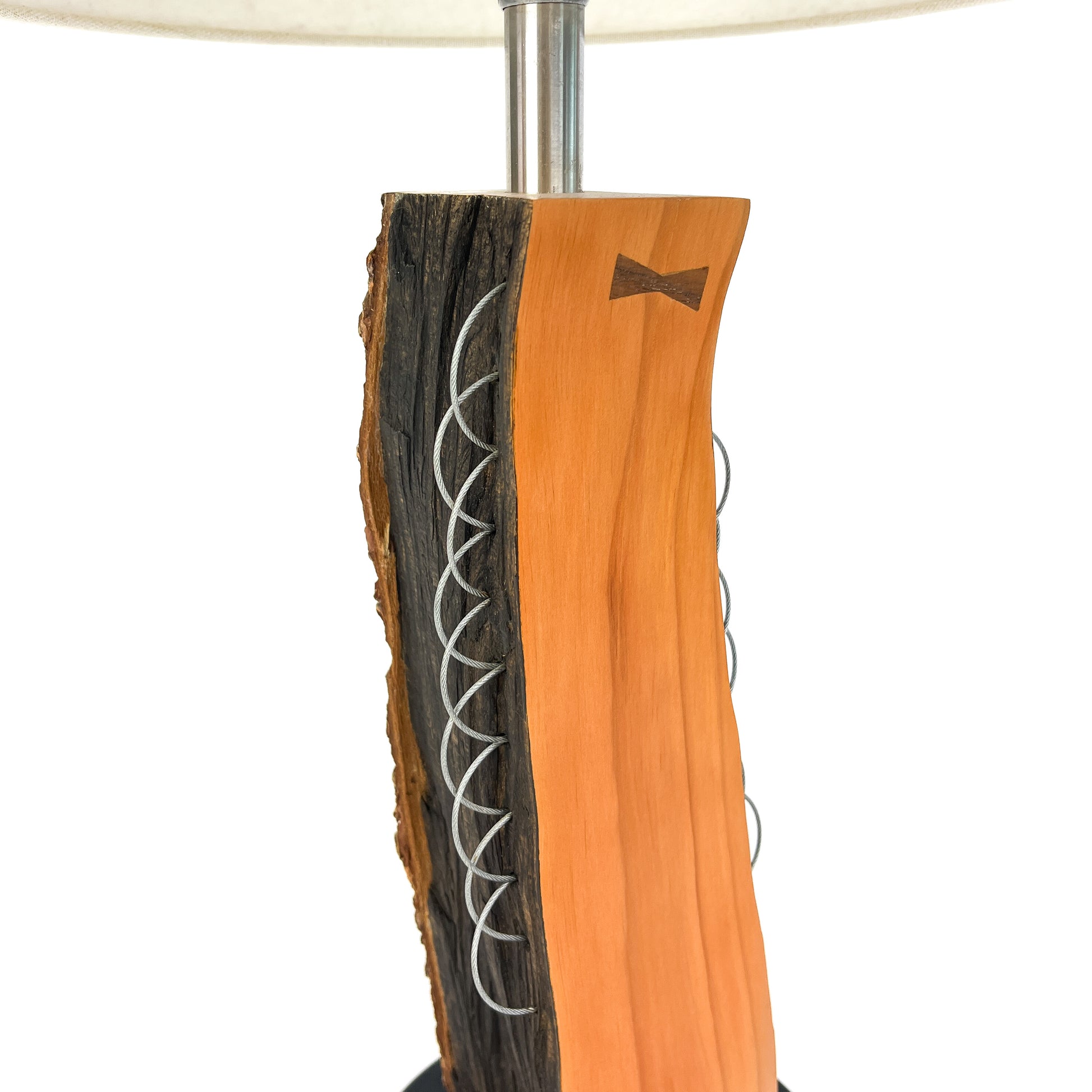 Close-up of a lamp base: dark wood with bark texture and metal string detail.